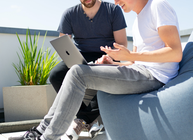 Deux hommes regardent un écran d'ordinateur portable sur une terrasse ensoleillée