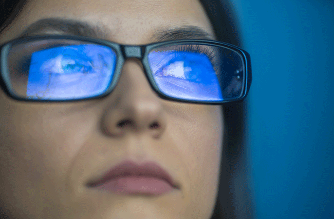 Bildschirm spiegelt sich in den Brillengläsern einer Frau.