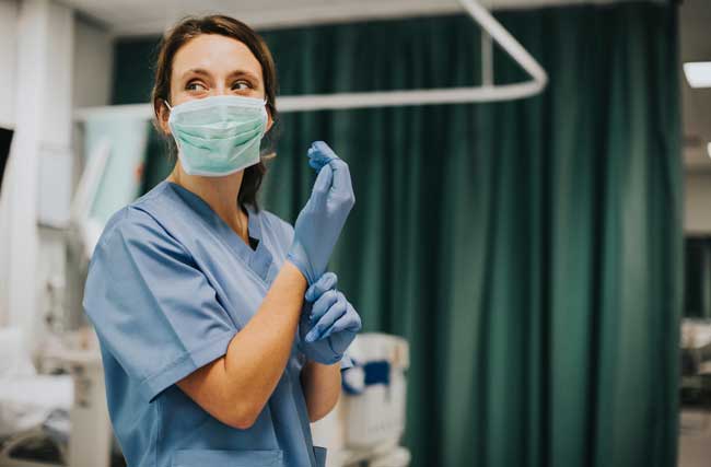 Krankenschwester mit Schutzmaske im Spital zieht Handschuhe an