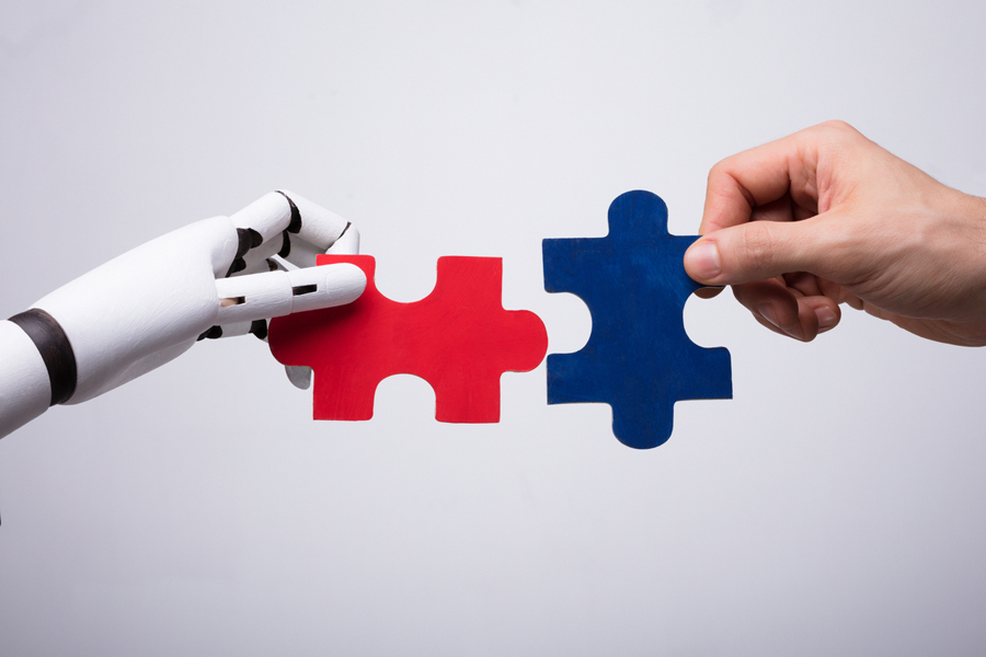 Une main robotique et une main humaine tiennent des pièces de puzzle