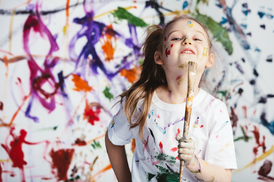 Une jeune fille se tient debout avec un pinceau devant un fond recouvert de peinture.