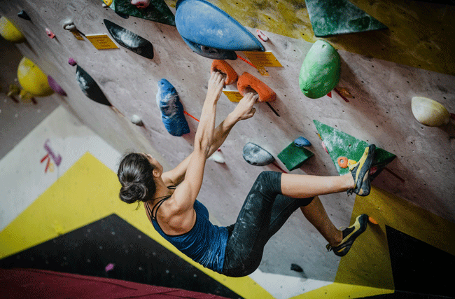 Junge Frau klettert eine Boulderwand hoch, die Herausforderung erfordert verschiedene Kompetenzen, ähnlich wie im Talentmanagement