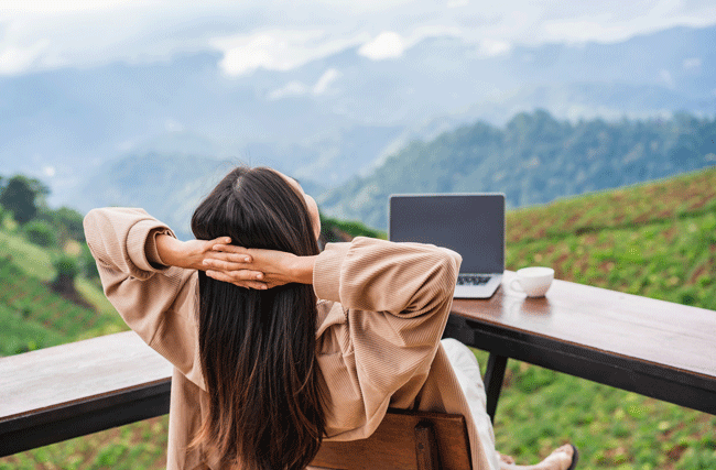 Eine Frau lehnt sich im Stuhl zurück und geniesst das Panorama vor ihr. Sie arbeitet zur Zeit auf Workation.