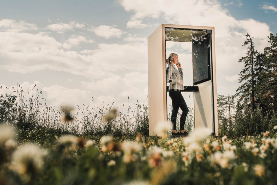 Une femme téléphone dans une cabine insonorisée au milieu d'une prairie