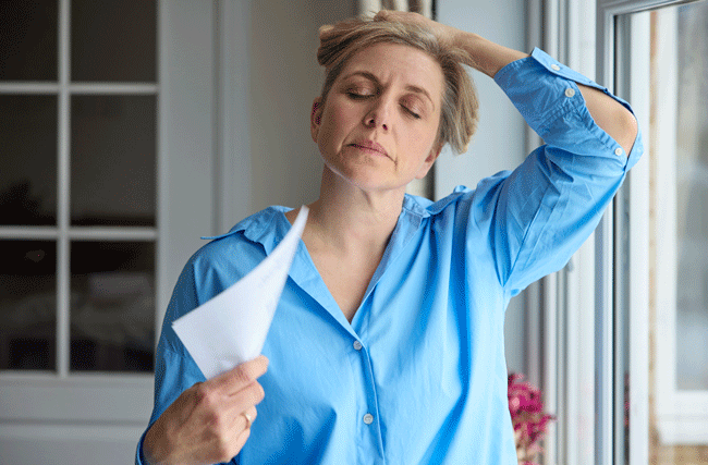 Frau in der Menopause fächert sich mit Papier. Studienergebnisse zu diesem Thema werden an der women's wellbeing summit präsentiert.