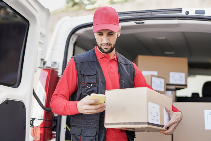 Un coursier utilise un smartphone alors qu'il tient une boîte de livraison devant sa camionnette