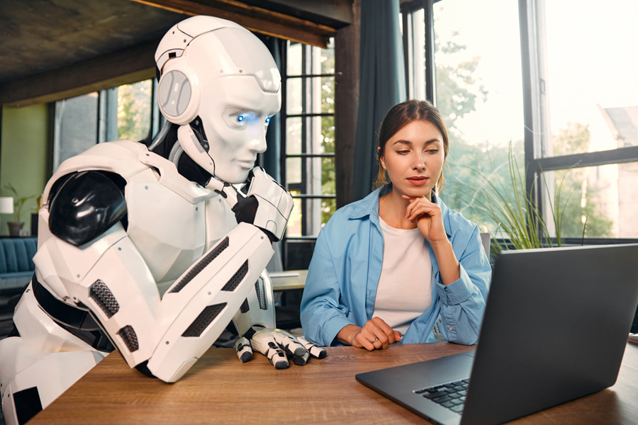 Une jeune femme et un robot humanoïde travaillent ensemble sur un ordinateur portable