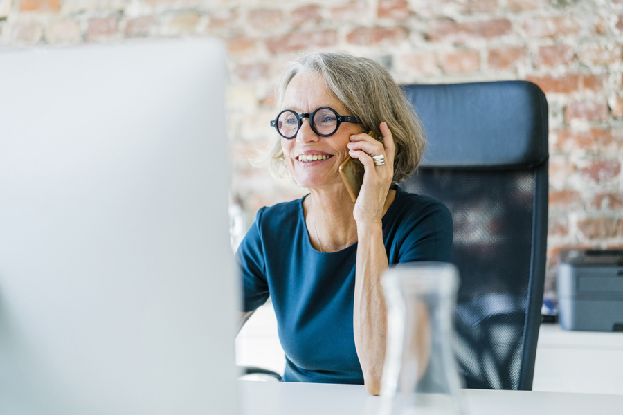 Une femme d'affaires senior assise à son bureau, utilisant un téléphone portable