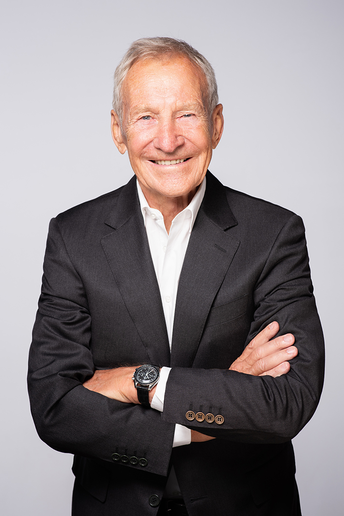 Das Bild zeigt Herbert Henzler, ein älterer Herr mit Jackett, weissem Hemd und Armbanduhr, gerade in die Kamera lächelnd.