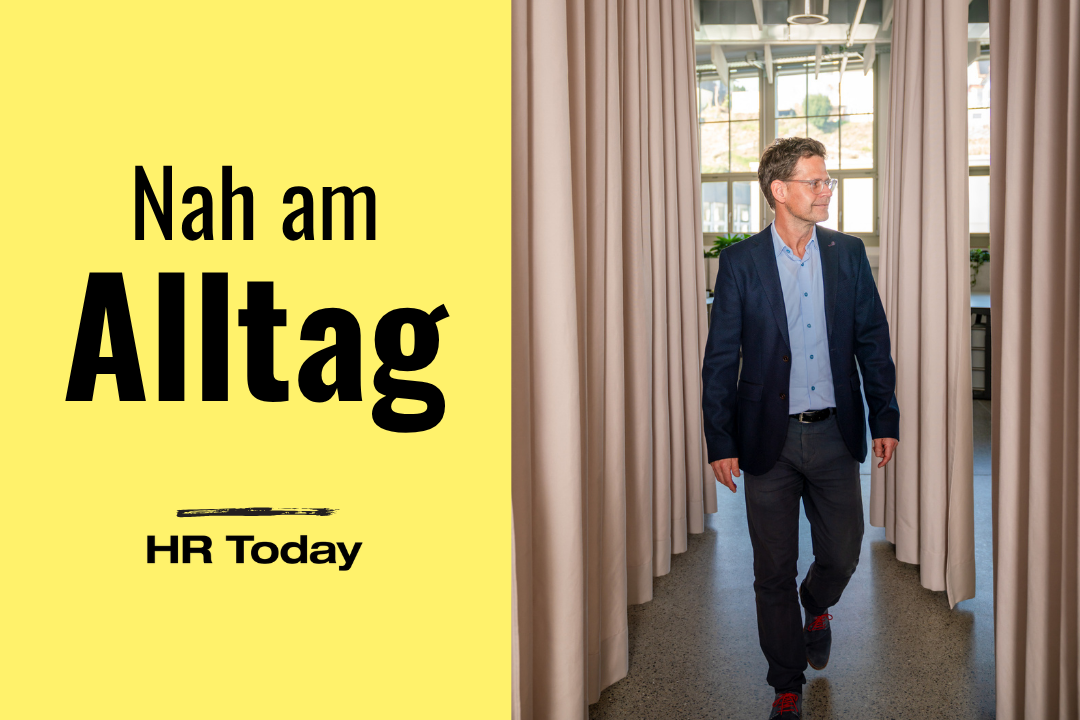 Das Bild ist vertikal geteilt. Links steht auf leuchtend gelbem Hintergrund der schwarze Text "Nah am Alltag", wobei "Alltag" groß und fett hervorgehoben ist. Die rechte Hälfte zeigt einen Mann mit Brille, hellblauem Hemd und dunkelblauem Sakko. Er geht zwischen zwei hellen, raumhohen Vorhängen in Richtung des Betrachters und blickt dabei nach rechts. Im Hintergrund sind große Fenster eines hellen Büroraums erkennbar.