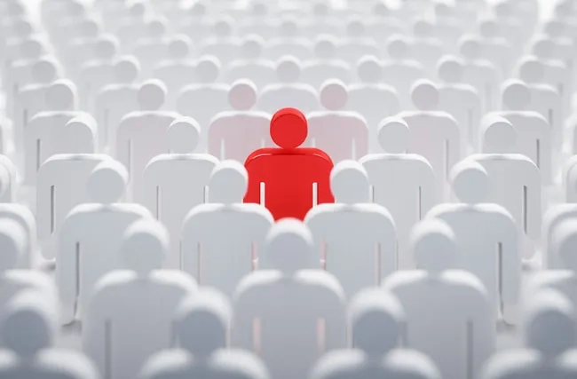 Symbolbild. Eine Mass von weissen Figuren. Darunter sticht eine knallrote Figur hervor, symbolisch für rare Fachkräfte mit Spezialwissen.