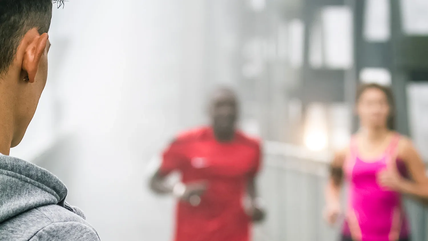 Das Bild zeigt eine leicht angeschnittene Person von schräg im Vordergrund, im Hintergrund zwei Sportler