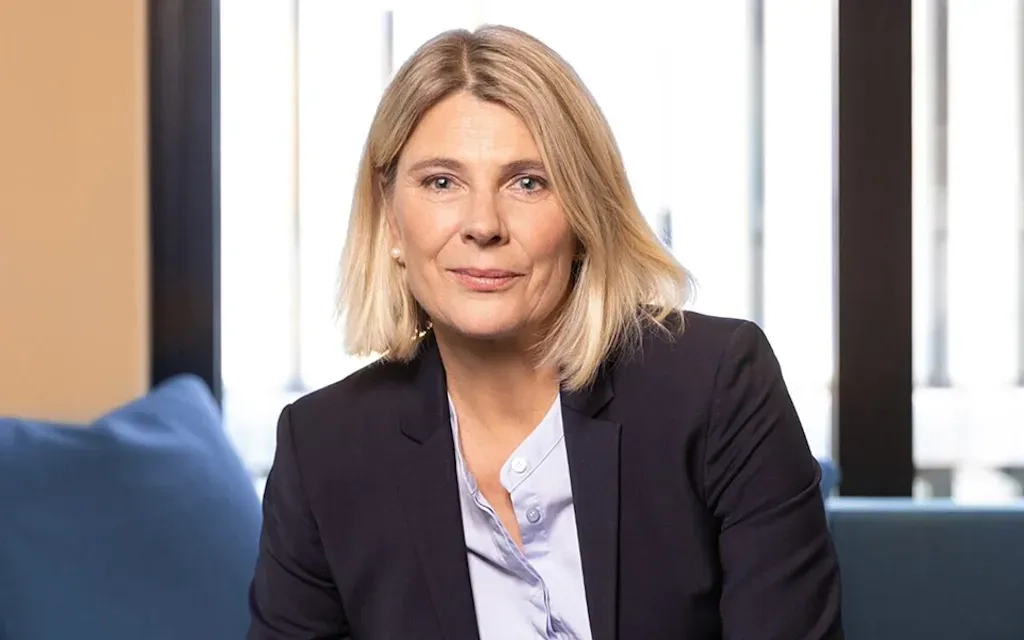 Das Bild zeigt Valérie Schelker, eine Frau mit blonden mittellangen Haaren, hellblauem Hemd und Blazer. 