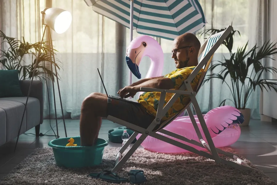 Un homme est assis sur une chaise longue dans le salon et travaille sur son ordinateur portable.
