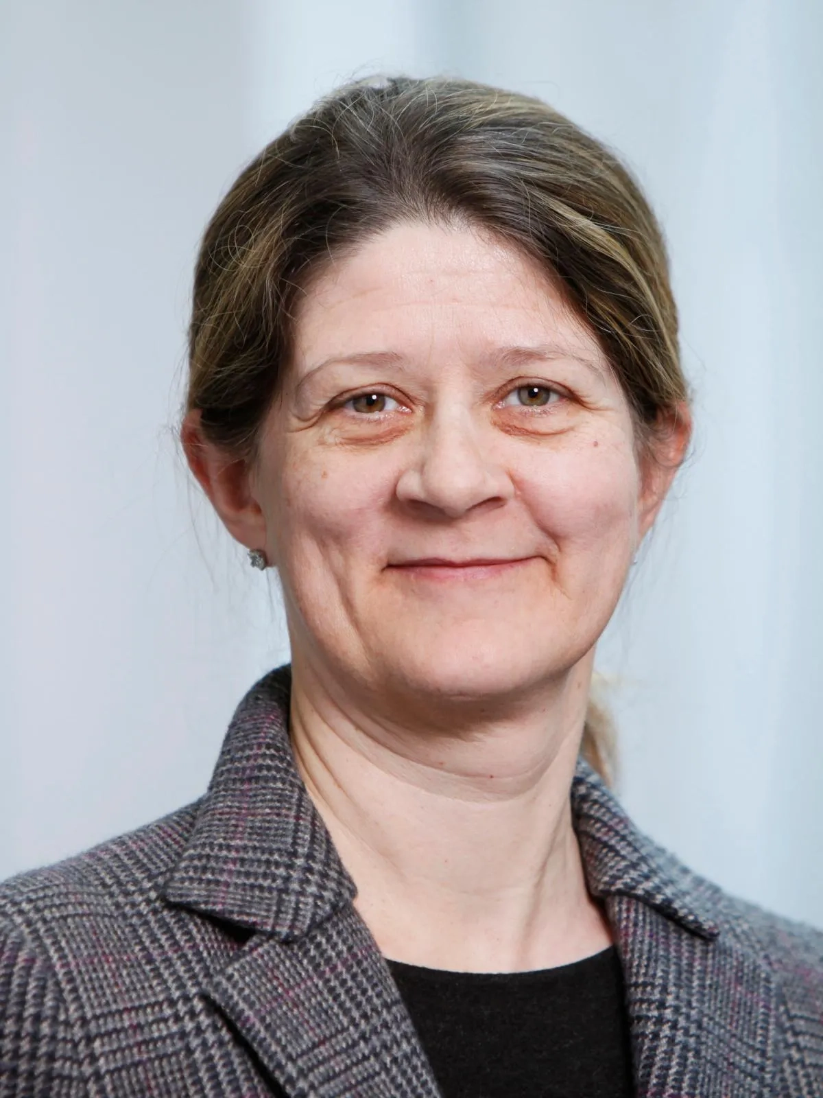 Porträtbild von Gudela Grote, sie lächelt leicht in die Kamera, trägt einen Blazer im Tweed-Stil und hat lange, hinten zusammengebundene braune Haare.